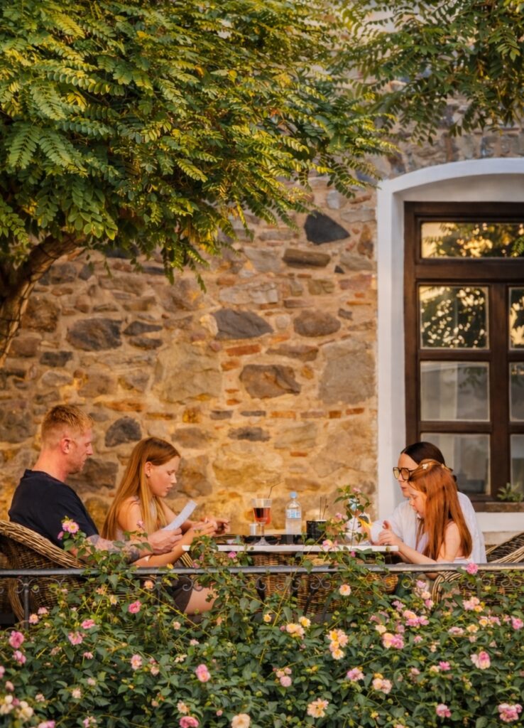Family enjoying drinks and light bites at a shaded garden terrace surrounded by flowers and greenery in Kardamena.