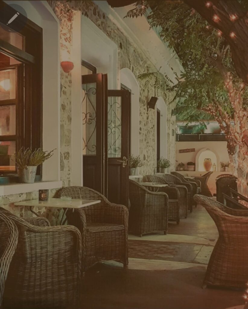 Romantic night view of The Garden Bar & Kitchen front terrace in Kardamena, featuring rustic stone walls, cozy seating, and trees illuminated by warm fairy lights.